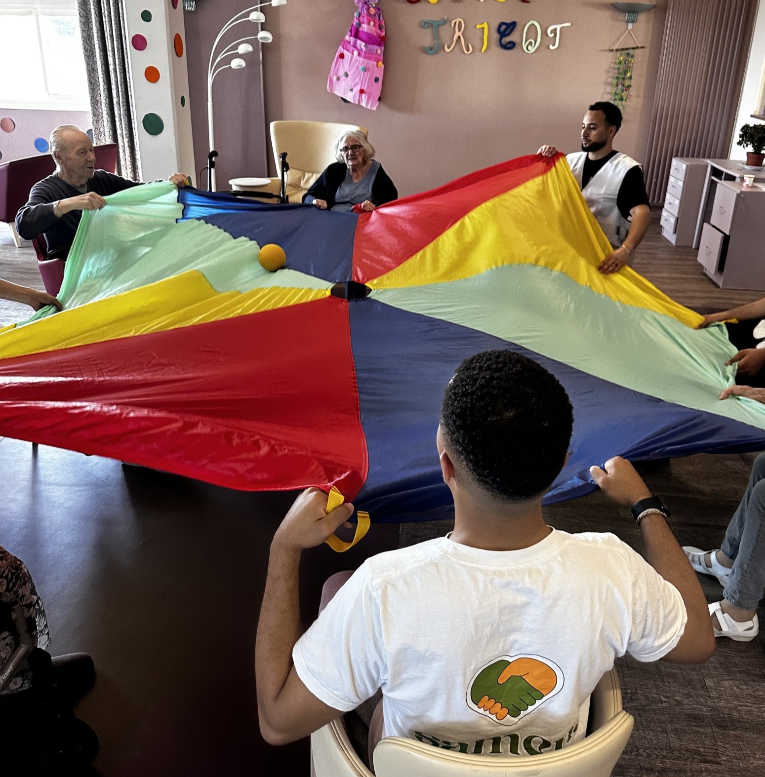 Des bénévoles de Samen animent un jeu de parachute coloré avec des résidents d'une maison de retraite.